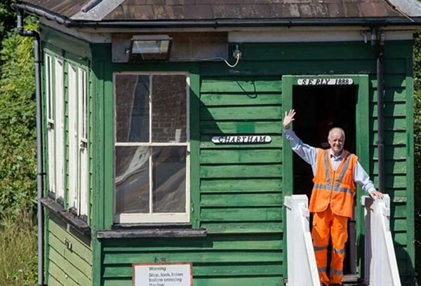Man in orange high vis closthing waving from the door of a signal box